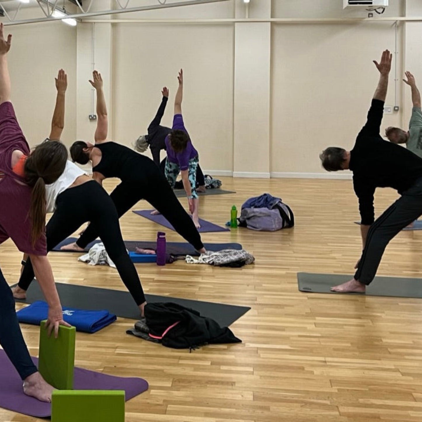 Group of people practicing yoga in a studio with mirrors on the wall.
