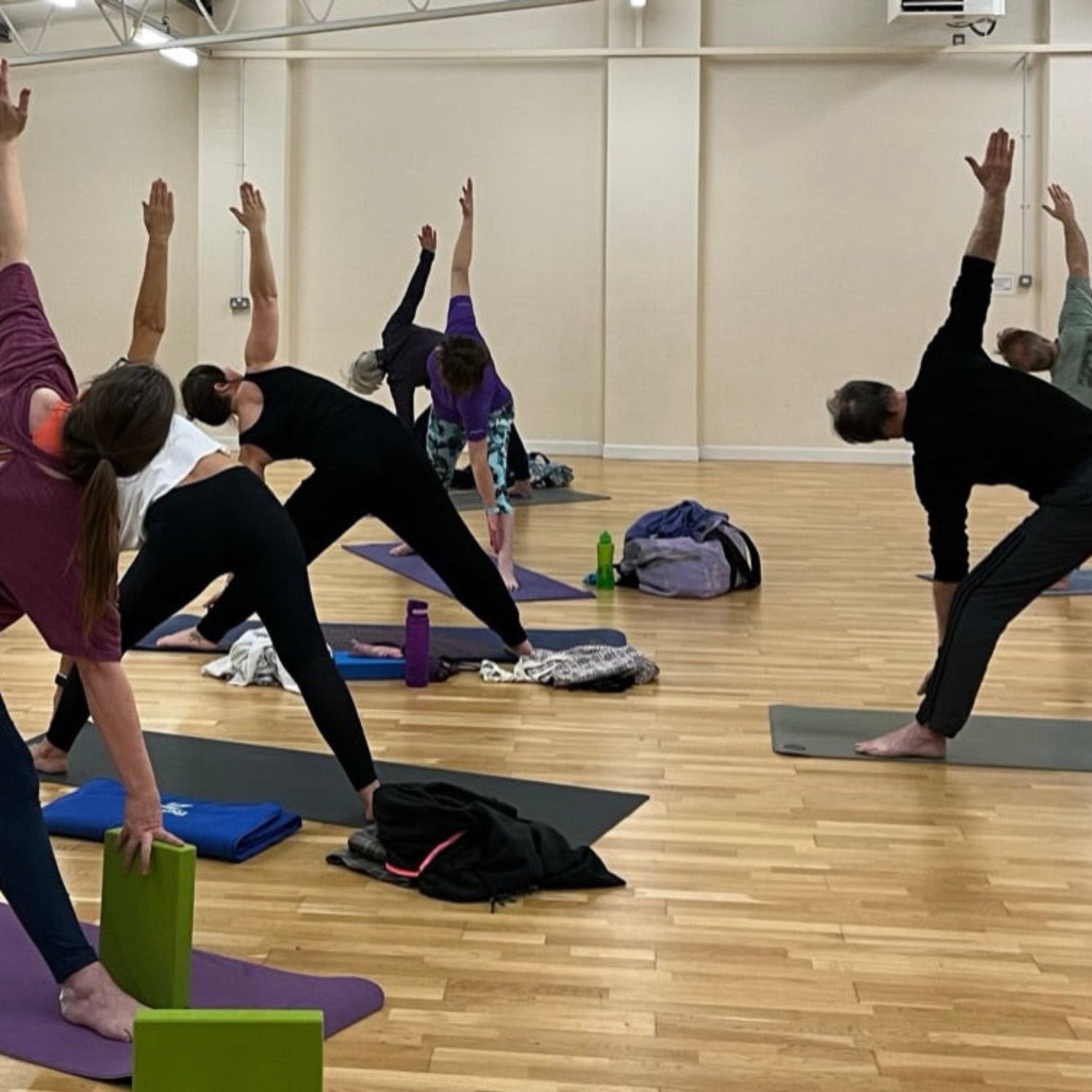 Group of people practicing yoga in a studio with mirrors on the wall.